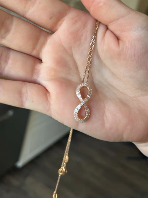 Swarovski hyperbola halsband - Säljer ett elegant halsband från Swarovski med ett infinity-symbol hänge i roséguld och gnistrande pärlor. Kedjan är tunn och stilren, perfekt för att lyfta din look med lite extra glans. Kommer i original ask. Liten fläck på askens lock (se sista bilden)