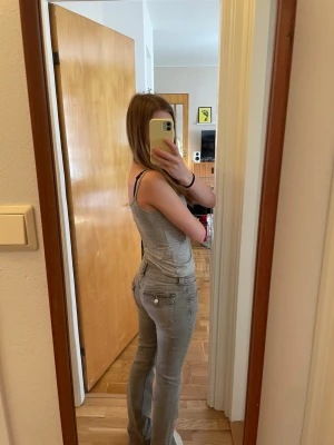 Gråa bootcut jeans med fickor - Säljer ett par gråa bootcut jeans med klassiska fem fickor och knappgylf. Jeansen har en snygg passform som sitter tight upptill och släpper vid benen. Perfekta för dig som gillar en enkel och stilren look. Ner till vid fötterna är det snören som sticker ut det är meningen, knappt använda!