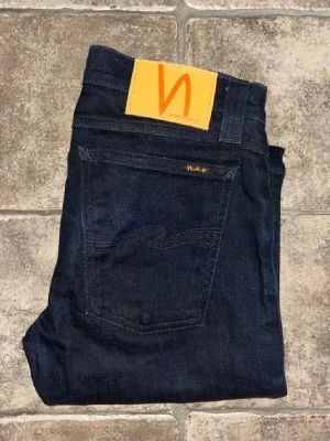 Nudie jeans  - Snygga mörkblå jeans från Nudie i modellen Tight Long John. De har en slim passform med smala ben och klassisk femficksdesign. Materialet är 99% bomull och 1% elastan för lite stretch. Midja 35cm, längd 105cm.  Ifall det inte finns någon bild i annonsen där jag bär plaggen jag säljer så är det för att jag ej kan ha storleken heller passformen, så kolla måtten för storlek och googla på modellnamnet för passform 😉 s4