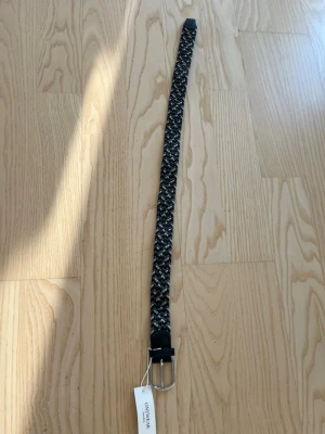 Flätat svart och grått bälte Onewear - Snyggt flätat bälte från Onewear i svart, grått och vitt. Bältet har ett klassiskt metallspänne och detaljer i svart skinn. Perfekt för att ge din outfit en cool touch.