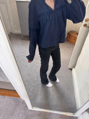 Mörkblå v-ringad blus med volym - Snygg mörkblå blus med v-ringning och generös volym i ärmarna. Blusen har långa ärmar med lätt puff och rynkade detaljer framtill. Tillverkad i ett tunt, mjukt tyg som ger en avslappnad men ändå chic look. Perfekt att styla med jeans eller kjol.
