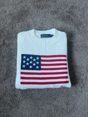 Vit stickad tröja Polo Ralph Lauren - Vit stickad tröja från Polo Ralph Lauren med amerikansk flagga på bröstet och RL- broderi. Endast testad, storlek S, vid frågor eller funderingar tveka inte på att höra av dig mvh 😁