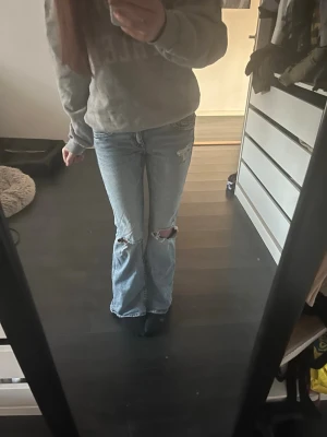 Ljusblå slitna bootcut jeans - Säljer ett par ljusblå bootcut jeans med slitningar och hål vid knäna. Jeansen har låg midja och klassiska fem fickor. Perfekta för en avslappnad och trendig look. Priset kan diskuteras!🥰