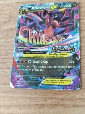 Pokémonkort Mega Garchomp EX & Lapras VMAX - Två samlarkort Pokémon: Mega Garchomp EX med färgstark design och texten CRIMSON samt Lapras VMAX med regnbågsglans och musiknoter. Båda korten har holografisk yta och detaljerade illustrationer. Perfekt för dig som gillar Pokémon och vill utöka din samling.