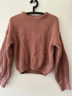 Rosa ribbstickad tröja - Mysig rosa ribbstickad tröja med rund hals och långa ärmar. Tröjan har en avslappnad passform och breda muddar vid ärmslut och nederkant. Perfekt för lager på lager och enkel att styla till jeans eller kjol. Lite lösa trådar här och var.