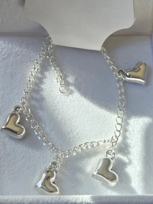 Silverfärgat armband med hjärtberlocker - Snyggt armband i silverfärgat rostfritt stål med fyra hjärtformade berlocker. Framsidan:med släta, blanka hjärtan och baksidan med glittriga, regnbågsskimrande hjärtan. Kedjan är tunn och justerbar för perfekt passform. Perfekt accessoar för att lyfta din stil.