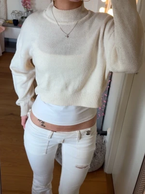 Vit cropped stickad tröja - Säljer en vit cropped stickad tröja från H&M Divided. Tröjan har hög hals, långa ärmar och ribbade muddar vid ärmslut och nederkant. 