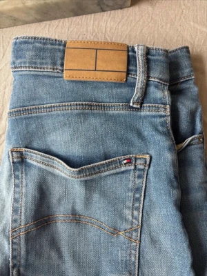 Ljusblå jeans shorts från Tommy Hilfiger - Säljer ett par ljusblå jeans shorts från Tommy Hilfiger i storlek 164. Passar en 13-14-årig kille.  Jeansshortsen är tillverkade i mjuk stretchig denims med snygga slitningar. Justerbar midja. Perfekta för en avslappnad och trendig look.