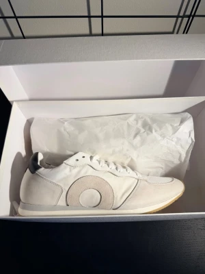 Oliver Cabell Runner Belmont - Helt nya vita sneakers från Oliver Cabell med grå mockadetaljer och ikonisk cirkel på sidan. Ovandel i läder och mesh med svart detalj på hälen samt slitstark gummisula. Stilren och minimalistisk design som passar till allt.  ✔ 100% äkta ✔ Helt nya ✔ Premium material ✔ Tidlös och stilren design