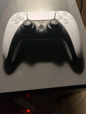 Sony DualSense PS5 handkontroll vit - Säljer en vit Sony DualSense handkontroll till PlayStation 5. Kontrollern har ergonomisk form, två analoga spakar, touchpad och klassiska PlayStation-knappar. Tillverkad i plast med modern design, perfekt för gaming.