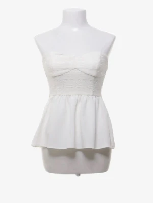 Vit axelbandslös peplum topp - Söt vit axelbandslös topp med peplumskärning och lätt struktur i tyget. Toppen har bandeau-formad överdel och markerad midja som ger en feminin siluett. Perfekt att styla med jeans eller kjol för en trendig look.