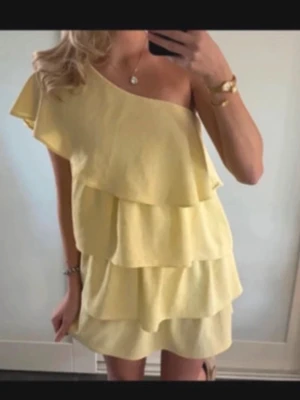 Gul volangklänning oneshoulder - Snygg gul kortklänning med flera volanger och oneshoulder-design. Klänningen har en luftig och somrig känsla med asymmetrisk axel och mjukt fall. Hör av dig om du har frågor 💞