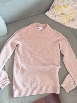 Beige stickad tröja från East West - Säljer en beige stickad tröja från East West i mjuk lammull. Tröjan har rund halsringning, ribbade muddar och nederkant samt en klassisk rak passform. Perfekt för lager på lager och riktigt skön att ha på sig. Provad två gånger 