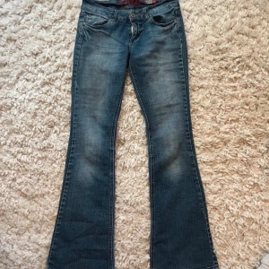 Blå bootcut jeans med broderade fickor - Säljer ett par blå bootcut jeans med snygg slitning och broderade detaljer på bakfickorna. Snygga och vintage från bongo. Lowrise jeans