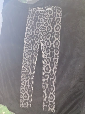Leopardmönstrade leggings i grått - Snygga leggings med leopardmönster i olika nyanser av grått och svart. De är stretchiga och har en smal passform som sitter tajt längs benen. Perfekta för dig som vill sticka ut med ett djuriskt print. Materialet känns mjukt och bekvämt mot huden.