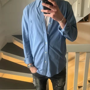 Blå skjorta från Ralph Lauren - Snygg blå skjorta från Ralph Lauren i featherweight mesh-material. Skjortan har långa ärmar och knappar framtill. Perfekt för en stilren look. Grabben på bilden är 180 lång. Den är sprillans ny aldrig använd fick den i present och fick inte me något kvitto men den är köpt på johnells. Nypris 1699kr. Två små hål som knappt syns se bild 5