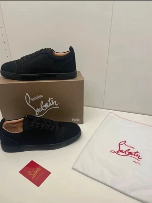 Svarta sneakers från Christian Louboutin - Stilrena svarta sneakers från Christian Louboutin i mocka med klassisk låg siluett. Skorna har svarta snören, diskret logga och beige innersula. Perfekta för dig som vill ha en clean och exklusiv look med lyxig känsla.