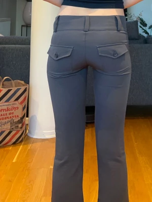 Grå kostymbyxor  - Snygga grå kostym byxor med låg midja och dekorativa fickor med knappar bak. Byxorna har bälteshällor och stängs med två knappar framtill. Materialet är stretchigt och bekvämt, storlek XXS 🫶🏼