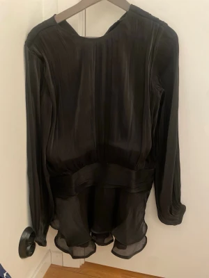 Svart volangklänning med lång ärm - PRIS KAN DISKUTERAS.                          Snygg svart kortklänning med volangkant och långärmade. Klänningen har en lös passform och är tillverkad i ett tunt, flygigt material som ger en elegant look. Perfekt för dig som gillar stilrena och trendiga plagg. Bara använd en gång💝 