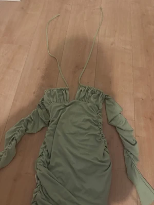 Ljusgrön omlottklänning med snörning - Trendig ljusgrön kortklänning med långa ärmar och snörning vid axlarna. Klänningen har omlottdetaljer och rynkade partier längs sidorna för en snygg passform. Perfekt för dig som vill sticka ut med en unik och modern look.