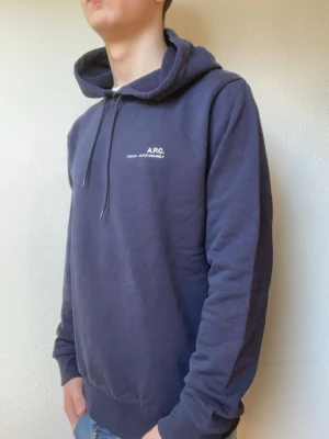 Mörkblå hoodie från A.P.C. - Snygg mörkblå hoodie från A.P.C. med liten vit logga och text på bröstet. Modellen på bilden är 178 och väger cirka 70kg. Modellen bär oftast S/M. Hör gärna av er vid funderingar eller frågor!