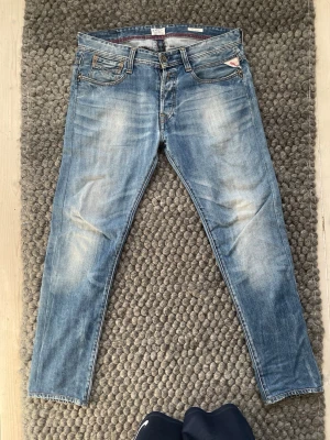 Blå Replay jeans med slitningar - Snygga blå jeans från Replay med klassisk femficksmodell och tydliga slitningar framtill. Jeansen har raka ben och röda detaljer på insidan av linningen. Tillverkade i bomull för en bekväm känsla.