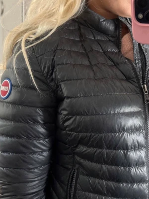 Svart dunjacka från Colmar - Säljer en svart dunjacka från Colmar med quiltad design och smal passform. Jackan har dragkedja framtill, två sidofickor med dragkedja och en rund Colmar-logga på ärmen. Perfekt för kalla vinterdagar och riktigt snygg till alla outfits. Storlek 44 barn så dam XS