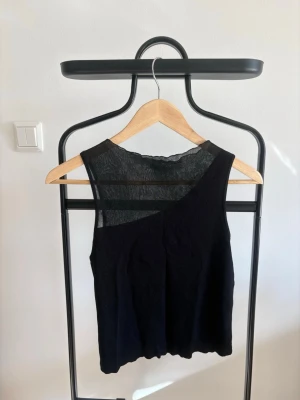 Svart topp från Zara - Snygg svart topp från Zara med transparent mesh upptill. Toppen är ärmlös och har en asymmetrisk skärning och stretchigt tyg. Den passar allt från S-L eftersom den formar sig! INTE uttöjd. Superfin och trendig!🌸