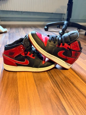 Air Jordan 1 High röd/svart - Säljer ett par klassiska Air Jordan 1 High sneakers i svart och rött läder med vita sulor. Skorna har den ikoniska Jumpman-loggan på plösen och Wings-loggan på sidan. Perfekta för dig som gillar streetwear och vill sticka ut med en tidlös modell. Går att gå ner i pris vid snabb affär