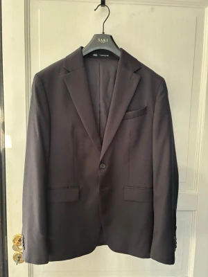 Zara Navy kostym - kemtvättad - strl. 46 - OBSERVERA: STORLEK PÅ BYXORNA ÄR 38. OBSERVERA: KOSTYMEN ÄR KEMTVÄTTAT OCH OANVÄND EFTER DETTA. Klassisk Navyblå kavaj från Zara Man med enkelknäppning och smala slag. Kavajen har två framfickor med lock, bröstficka och knappar vid ärmsluten. Perfekt för en clean och dressad stil.