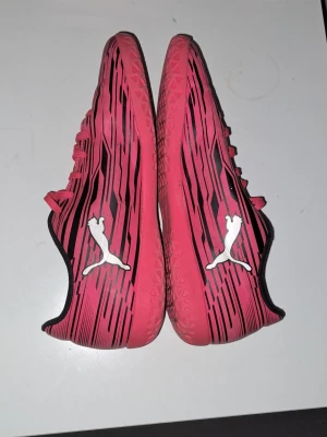 Inomhusskor Puma - Säljer ett par snygga röda inomhus skor från Puma med svart och vitt mönster samt den klassiska Puma-loggan i vitt på sidan. Skorna har snörning och en låg profil, perfekta för snabba rörelser. På insidan är svart för extra kontrast.