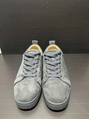 Gråa sneakers från Christian Louboutin - Snygga gråa sneakers från Christian Louboutin i mocka med matchande grå skosnören och diskret design. Låg modell med klassisk siluett och exklusiv känsla. Perfekta för dig som vill ha stilrena och lyxiga skor i garderoben.