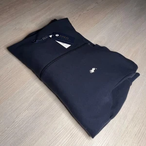 Mörkblå Ralph Lauren zip - Säljer en stilren zip hoodie från Polo Ralph Lauren färgad mörkblå. Tröjan är i storlek M och är köpt för cirka 2500kr, väldigt goo till våren