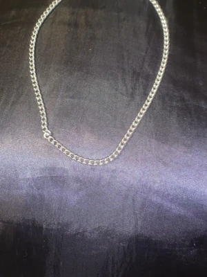 Silverfärgat kedjehalsband - Stilrent halsband i silverfärg med klassisk kedjedesign. Halsbandet har rundade länkar som ger en enkel men snygg look. Perfekt att bära som det är eller att kombinera med andra smycken för en personlig stil.