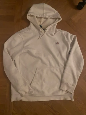 Vit hoodie från Dickies - Snygg vit hoodie från Dickies med klassisk logga på bröstet. Hoodien har en stor ficka framtill och justerbar huva med snören. Tillverkad i mjukt material som känns skönt mot huden. Perfekt för en avslappnad och stilren look.