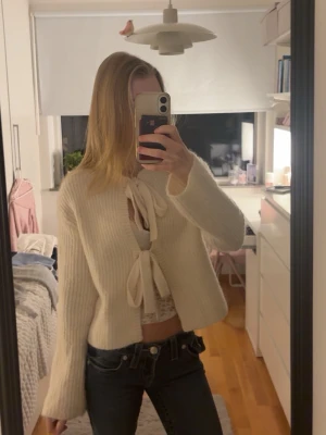 Krämvit kofta med knyt från Gina Tricot - Superfin krämvit ribbstickad kofta från Gina Tricot med två stora knytband framtill, perfekt att knyta till rosetter. Den har långa ärmar och rund halsringning. 