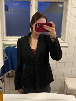 Svart kavaj från Amanda Marshall med markerad midja - Snygg svart kavaj med markerad midja och klassisk krage. Kavajen har ett diskret sömmönster längs kanterna och stängs med en knapp framtill. Perfekt för en stilren och trendig look. Materialet är slätt och fodrat för extra komfort. Oversized