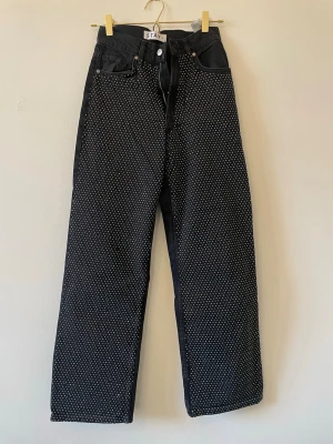 Svarta jeans med pärldetaljer från STAY - Unika svarta jeans från STAY i storlek XS med raka ben och hög midja. Jeansen är dekorerade med små pärlor över hela framsidan som ger en cool och trendig look. Klassisk femficksmodell och knappgylf. 