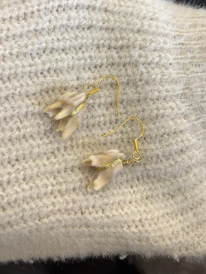 Unika örhängen med guldfärgade krokar - Säljer ett par unika örhängen med guldfärgade krokar och hängande tänder. Örhängena har en organisk form och är handgjorda, vilket ger dem en cool och personlig look. Perfekt för dig som gillar annorlunda accessoarer.