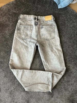 Ljusgrå jeans från GANT - Snygga ljusgrå jeans från GANT med klassisk femficksmodell och relaxade ben. Jeansen har bälteshällor, knappgylf och är tillverkade i ett mjukt denimtyg. Perfekta för en avslappnad och trendig look. Storlek 170 15 år