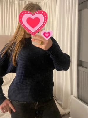 Mörkblå ribbstickad tröja - Mysig mörkblå stickad tröja med ribbad struktur och rund hals. Tröjan har långa ärmar och en avslappnad passform, perfekt för kyliga dagar. Passar till både jeans och kjol för en enkel och snygg look.