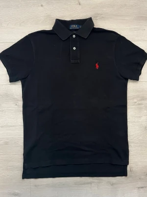 Ralph lauren pike svart - Säljer en klassisk svart piké från Ralph Lauren. En stilren och tidlös modell som passar till i princip allt och är ett självklart plagg i garderoben.  • Storlek: M • Färg: Svart • Skick: Mycket fint skick • Broderad Ralph Lauren-logga på bröstet • Mjuk och bekväm passform • Perfekt att matcha med jeans, chinos eller shorts • Passar lika bra till vardag som till mer uppklädda tillfällen