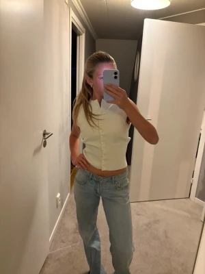 Vit ärmlös blus med knappar - Stilren vit ärmlös blus med krage och knäppning framtill. Toppen är croppad och har en klassisk, clean look som passar perfekt till jeans eller kjol. Enkel att styla för en trendig vardagsoutfit.