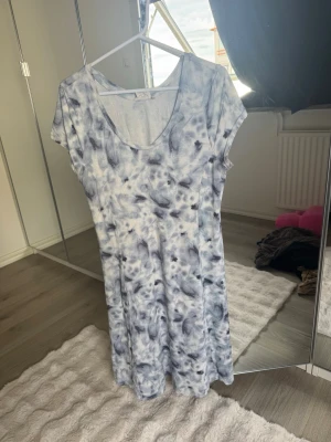 Blåvit mönstrad kortklänning - Säljer en blåvit kortklänning med coolt batikmönster. Klänningen har korta ärmar och en rundad urringning. Perfekt för dig som gillar en avslappnad och trendig stil. Materialet känns mjukt och skönt mot huden.