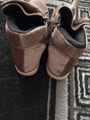 Rosa sammetsneakers med rosett - Unika sneakers i rosa sammet med stora dekorativa rosetter framtill och dragkedja på sidan. Skorna har en vit sula och svart innerfoder. Perfekta för dig som vill sticka ut med en trendig och annorlunda look.