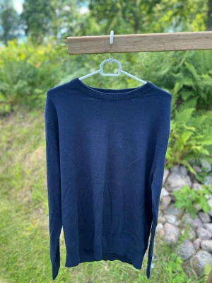 Mörkblå stickad tröja - En enkel och stilren mörkblå stickad tröja med rund halsringning och långa ärmar. Tröjan har ribbade muddar vid ärmslut och nederkant. Perfekt att slänga på sig när det är lite kyligt ute.