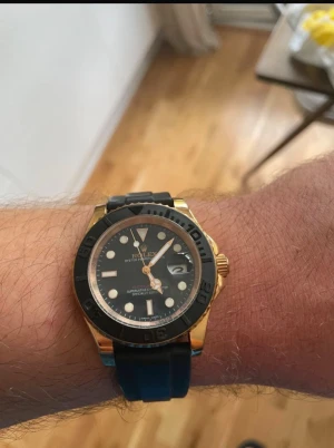 Rolx Yacht-Master. Skriv bara för att diskutera pris  - Snygg rolx Yacht-Master klocka med svart urtavla, guldtonad boett och svart vridring. Klockan har tydliga indexmarkeringar, datumfönster och svart gummiband som ger en sportig känsla. Perfekt accessoar för dig som gillar exklusiv stil.