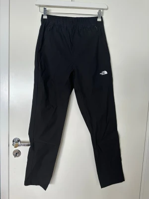 Svarta mjukisbyxor från The North Face - Säljer ett par svarta mjukisbyxor från The North Face med resår i midjan och diskret logga på vänster ben. Byxorna har raka ben och sidofickor med dragkedja. Perfekta för chill eller träning, tillverkade i ett mjukt och lätt material.