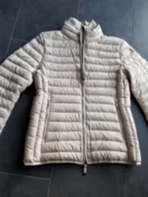 Beige dunjacka från Parajumpers - Snygg beige dunjacka från Parajumpers med quiltad design och hög krage. Jackan har dragkedja framtill, två sidofickor med dragkedja och en patch med logga på ärmen. Perfekt för kalla vinterdagar och riktigt lätt att bära.