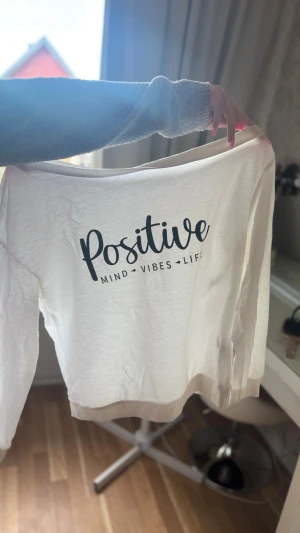 Vit sweatshirt med tryck 'Positive' - Vit sweatshirt med svart text på ryggen: 'Positive Mind Vibes Life'. Tröjan har rund halsringning, långa ärmar och ribbade muddar vid ärmslut och nederkant. Tillverkad i mjukt bomullsliknande material. Perfekt för en chill och avslappnad stil.